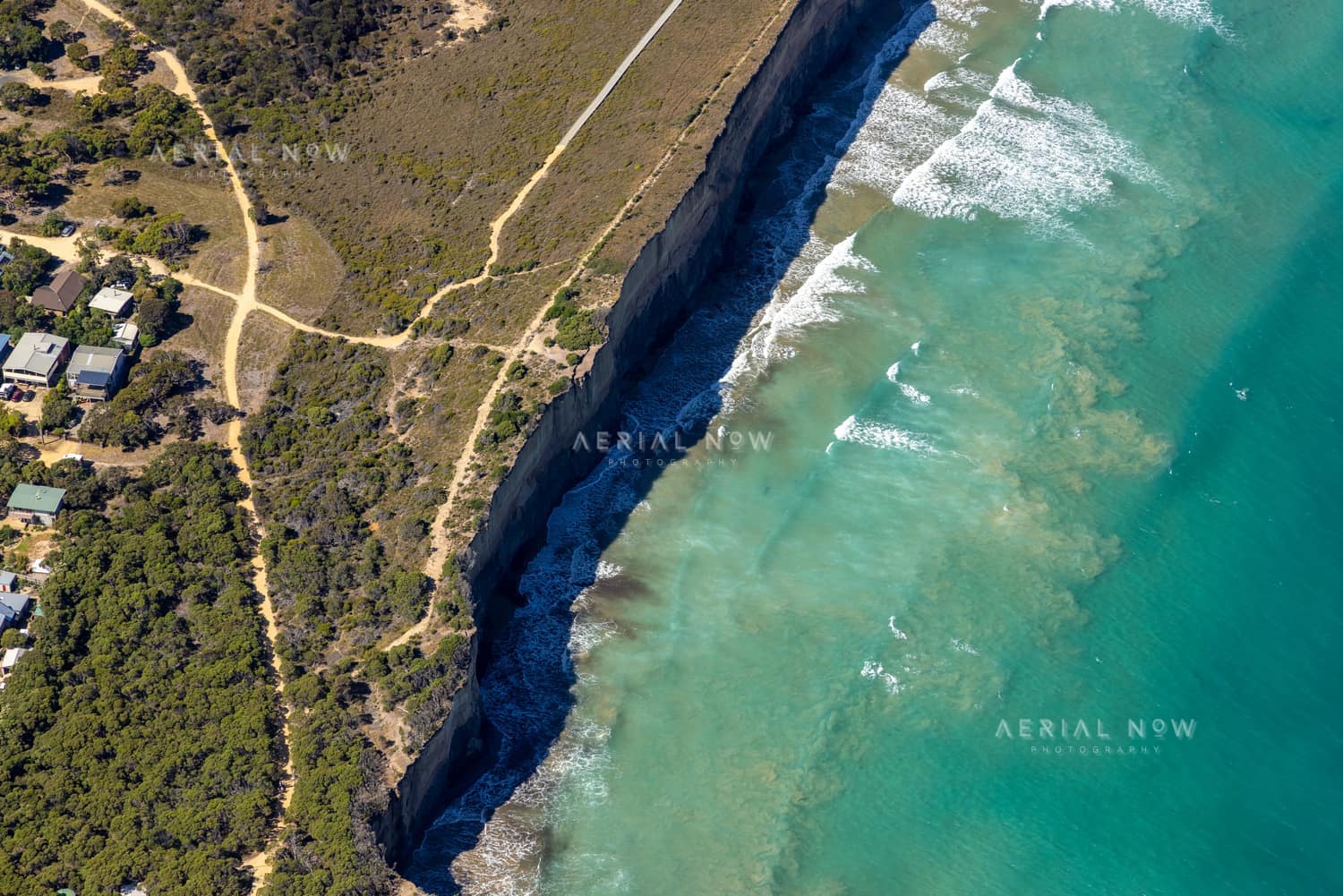 Aerial view of Anglesea cliffs beside Bass Strait, with turquoise water, breaking waves, coastal scrub, walking tracks and nearby houses in Anglesea VIC.