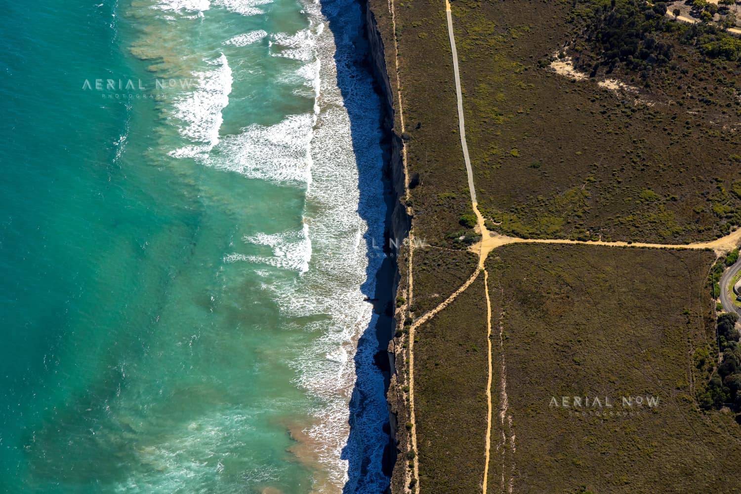 Aerial view of the Anglesea ocean cliffs beside Bass Strait, with turquoise surf, wave lines, coastal heathland and sandy walking tracks in Anglesea Victoria.