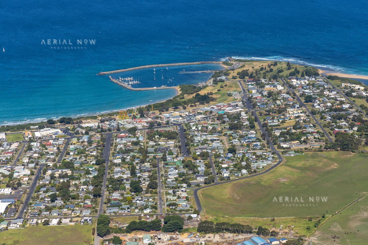 Aerial view of Apollo Bay Harbour, the coastline and surrounding township streets and homes in Apollo Bay, Victoria.