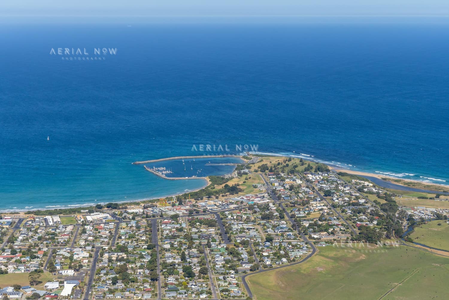 Aerial view of Apollo Bay Harbour with breakwaters, marina berths, coastal homes, beaches and the Southern Ocean at Apollo Bay VIC.
