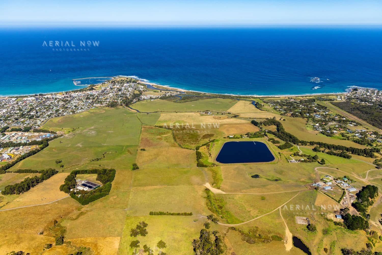 Aerial view of Apollo Bay coastline with farmland, township areas, a small reservoir and the blue ocean in Apollo Bay, Victoria.