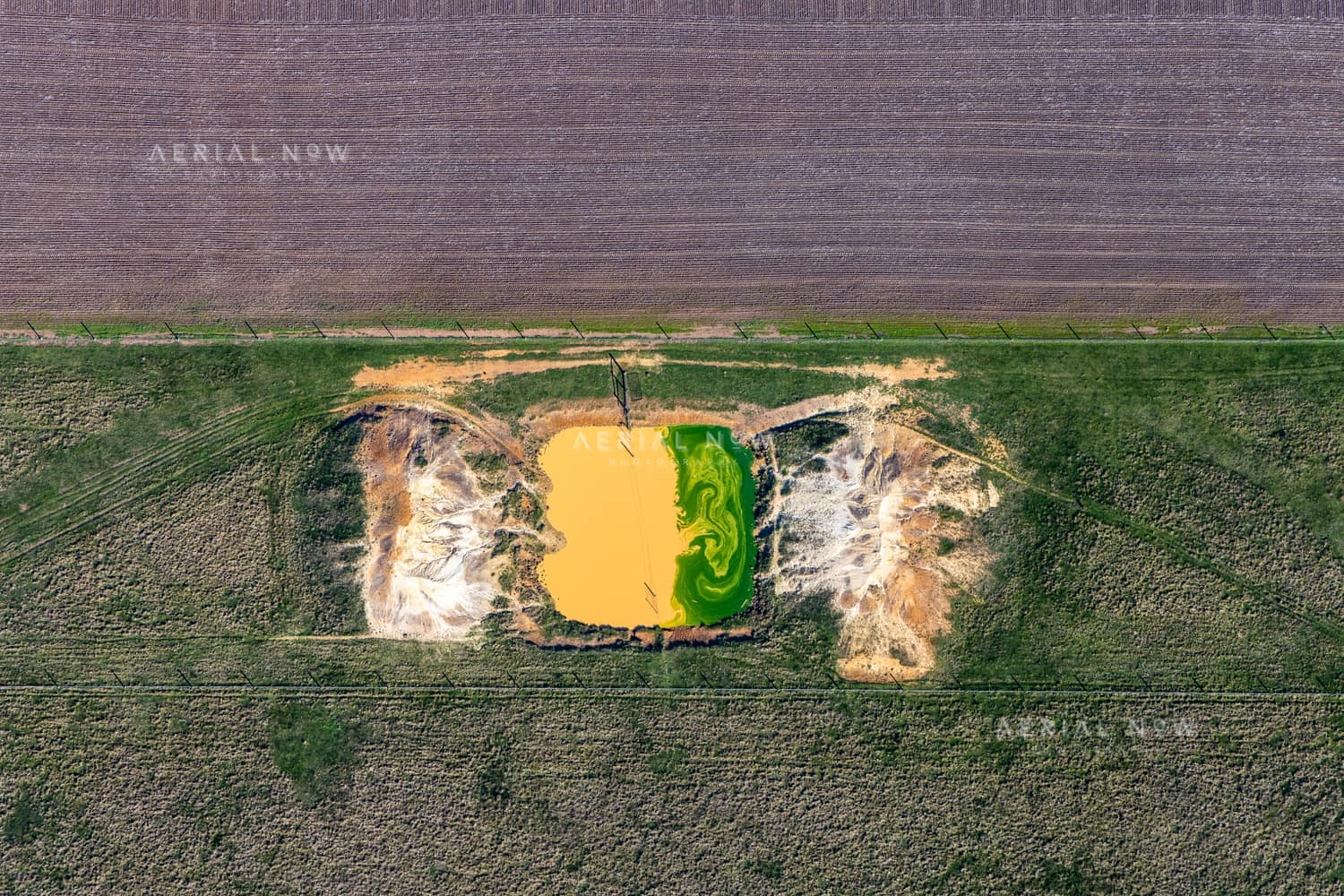 Aerial view of a small farm dam with green algae beside exposed earthworks and surrounding paddocks near Bannockburn, Victoria.