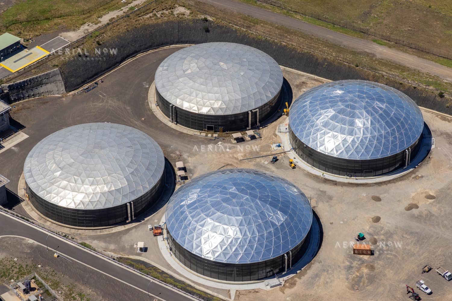 Aerial view of four large covered utility process tanks with faceted membrane roofs, access roads, earthworks and service vehicles in Craigieburn, Victoria.