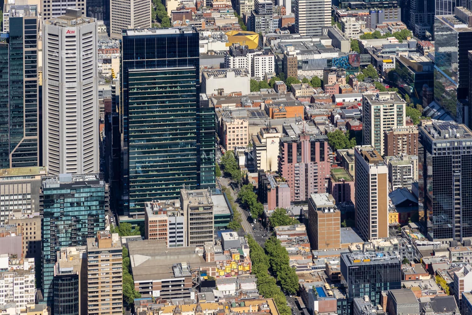 Aerial view of high-rise office towers and apartment buildings in Melbourne CBD, with dense city blocks, street trees and visible Aon signage.