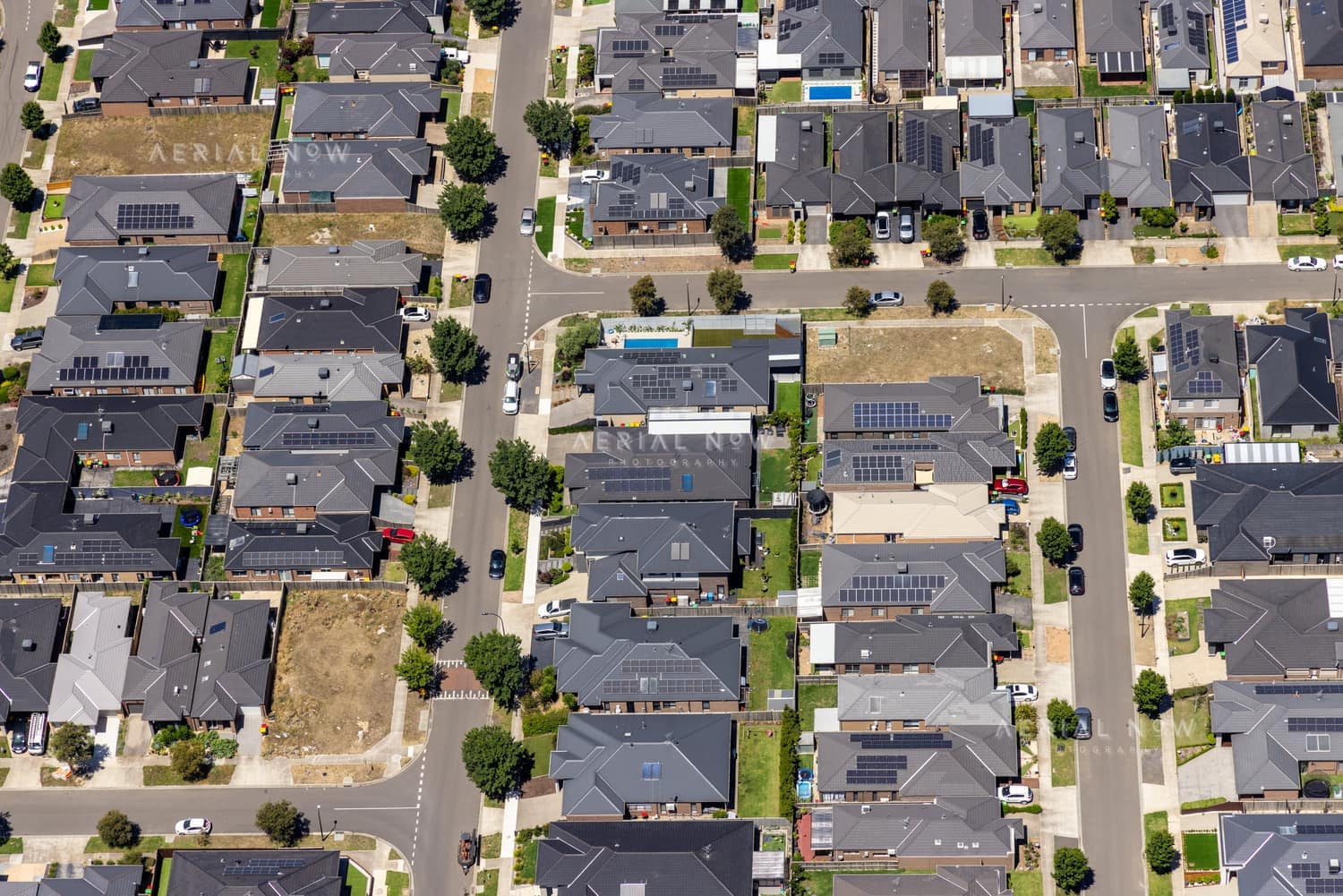Aerial view of the Hollington Drive housing estate in Mickleham VIC, showing modern suburban homes, rooftop solar panels, residential streets, parked cars and vacant lots.