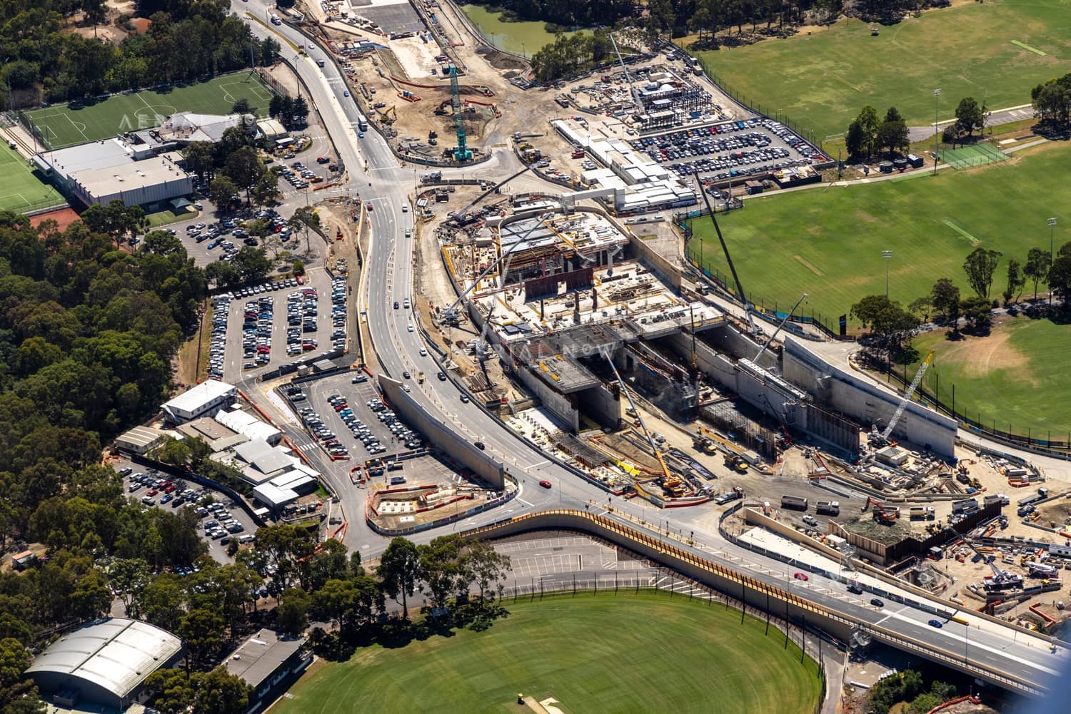 Aerial view of road and bridge construction beside sports fields, car parks and surrounding streets in Balwyn North, Victoria.
