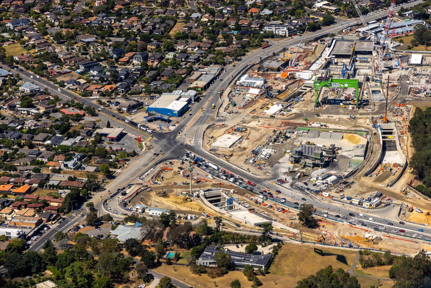 Aerial view of North East Link construction in Heidelberg, showing major roadworks, excavation areas, site compounds, traffic and surrounding residential streets.