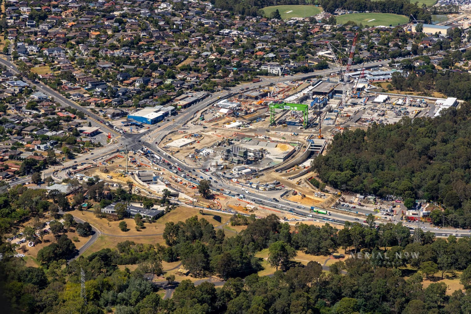 Aerial view of the North East Link construction site in Heidelberg, showing roadworks, construction zones, suburban streets, parkland and surrounding residential areas.