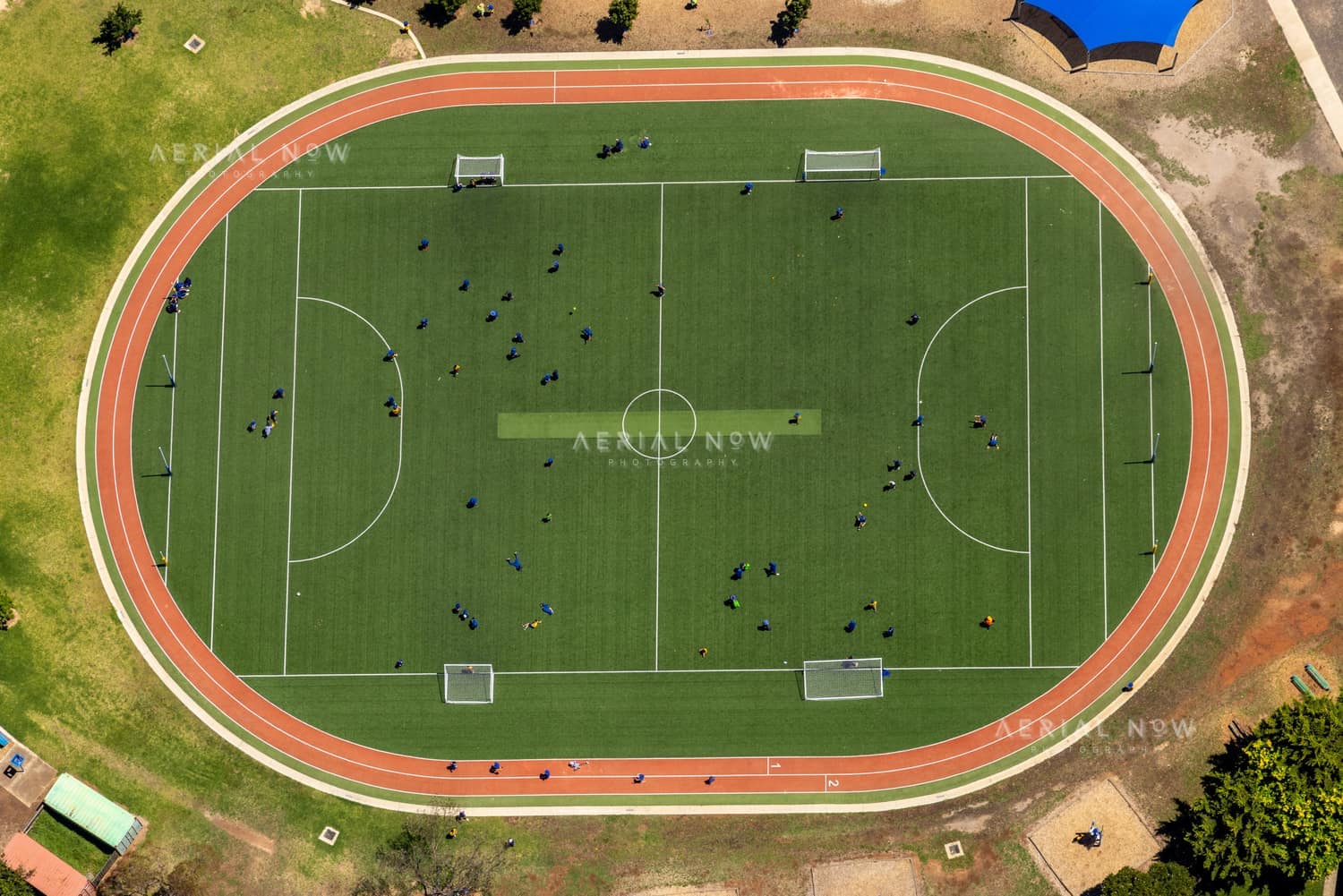 Aerial view of a soccer field with goalposts, player groups and a surrounding red athletics track near Astor Place in Melton West, Victoria.