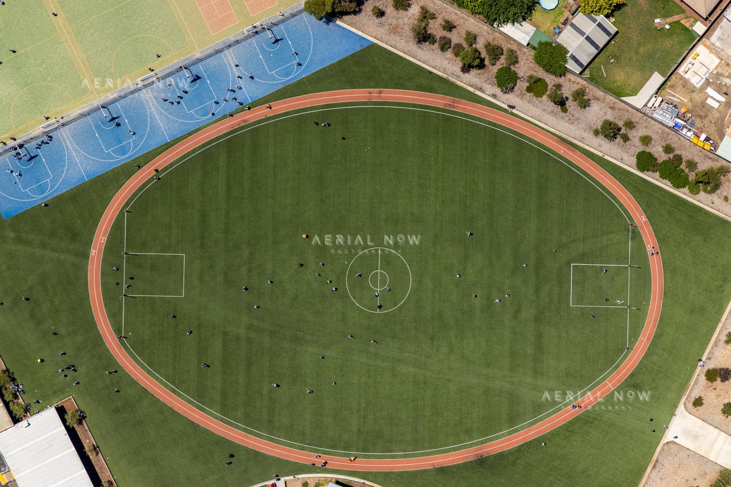 Aerial view of the sports oval, running track markings and blue hard courts beside Wedge Park Primary School on Cambrian Way in Melton West, Victoria.