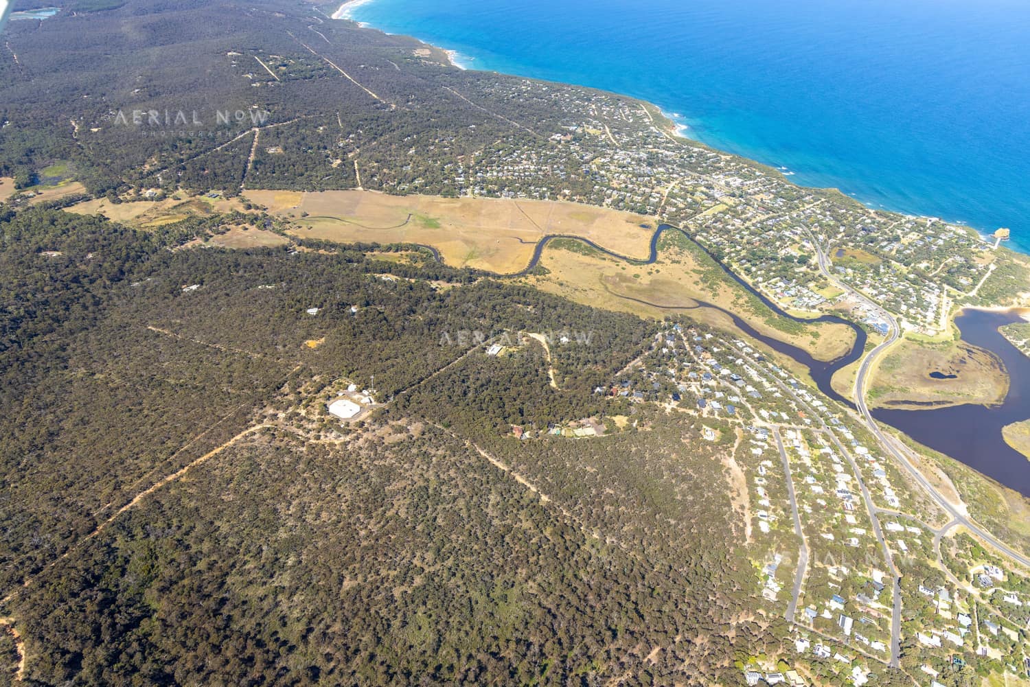 Aerial view of Painkalac Creek winding through estuary wetlands beside coastal housing, bushland and the Surf Coast shoreline at Aireys Inlet and Fairhaven in Victoria.