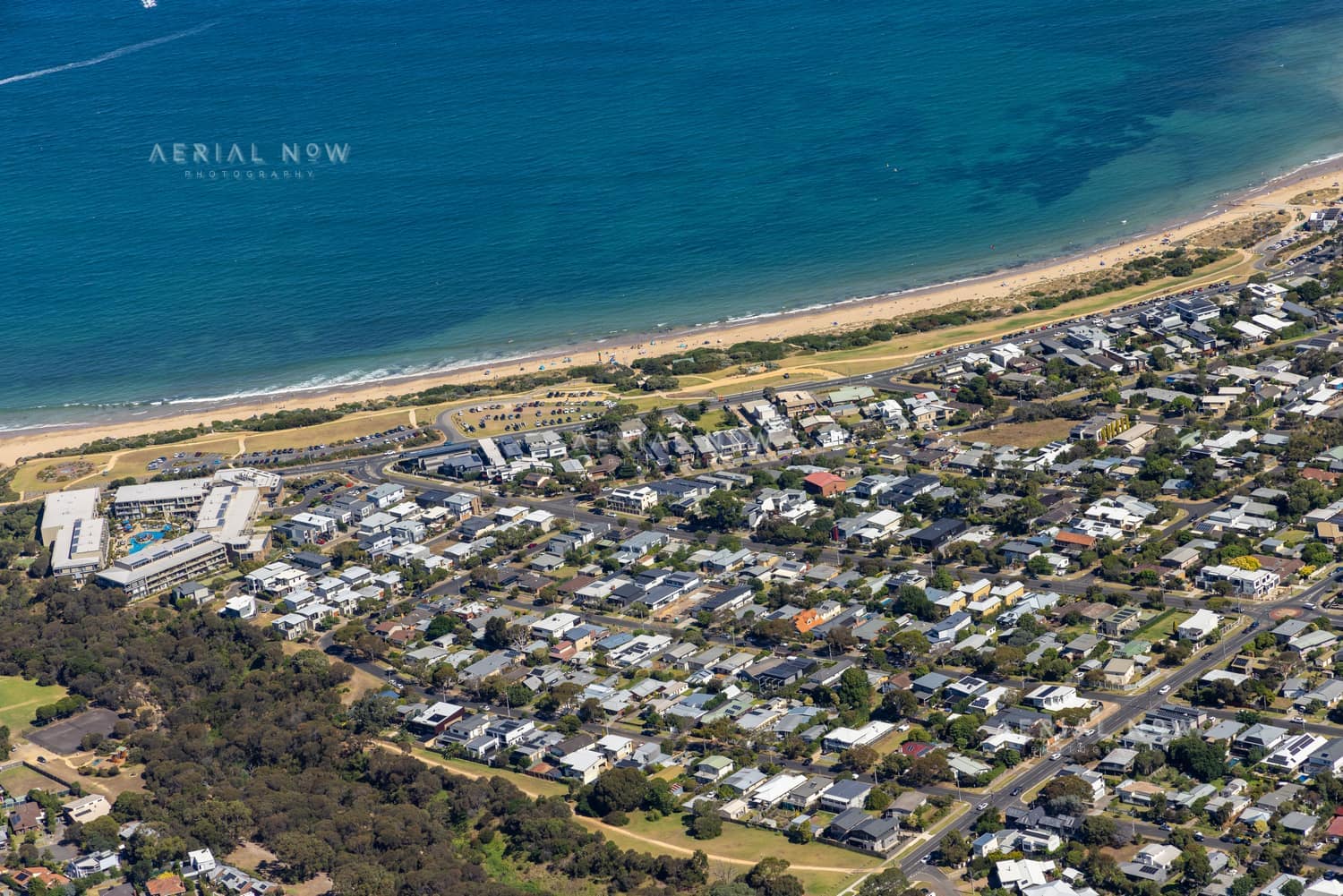 Aerial view of Fishermans Beach and The Esplanade at Torquay, with beachfront homes, resort buildings, coastal road, sandy shoreline and blue water.