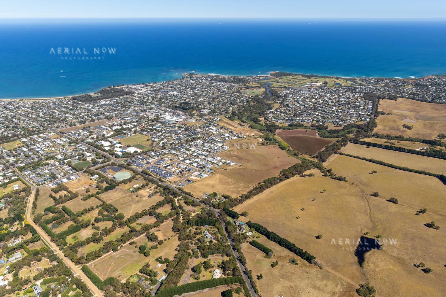 Aerial view of Torquay VIC showing the coastline, ocean, residential estates, farmland and green creek corridor.