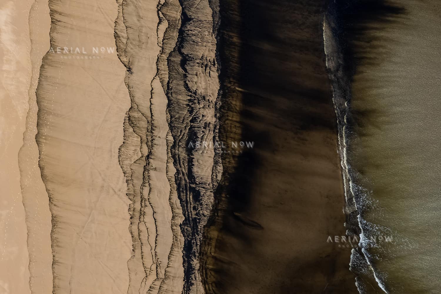 Aerial view of abstract sand, tidal debris and dark shoreline patterns on Inverloch Beach beside Bass Strait in Victoria.