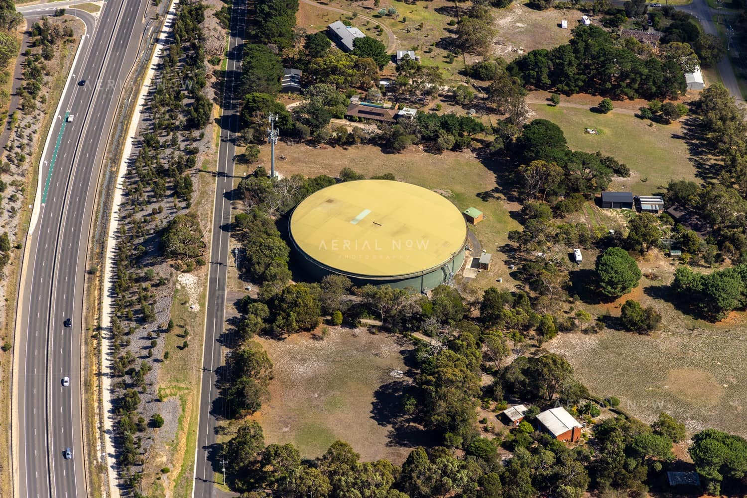 Aerial view of a large circular water storage tank near Andersons Road in Drysdale, with surrounding rural properties, trees and adjacent road traffic.