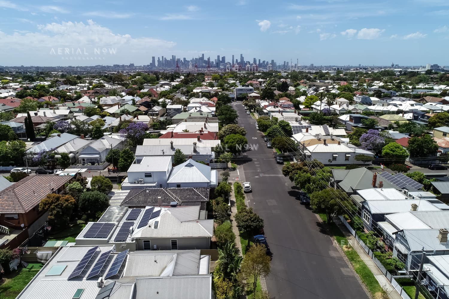 Aerial view over residential streets and rooftops in Yarraville, with the Melbourne CBD skyline visible in the background.