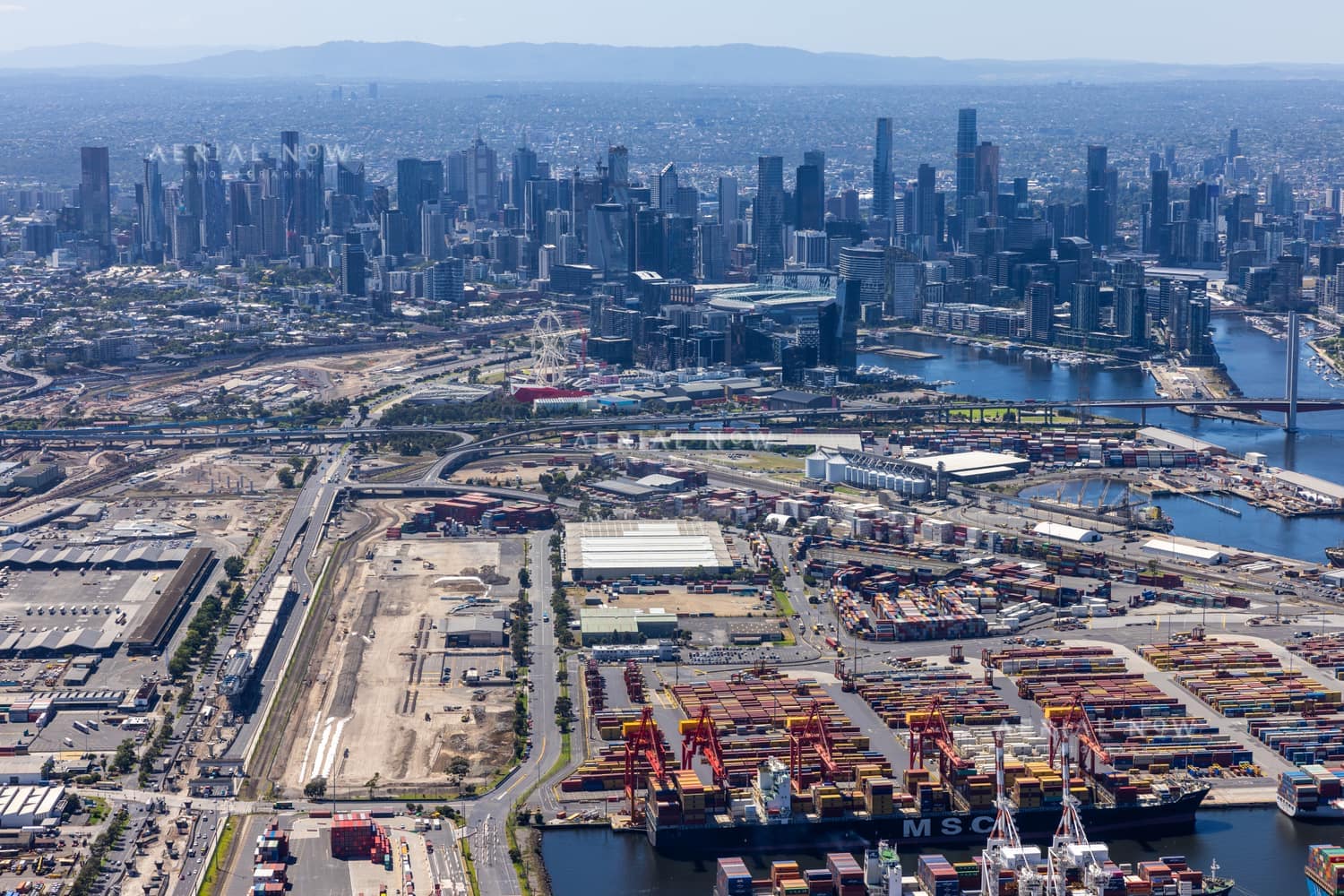 Aerial view of Port of Melbourne container terminals, the Port Rail Transformation Project construction site, Bolte Bridge and the Melbourne CBD skyline in February 2022.