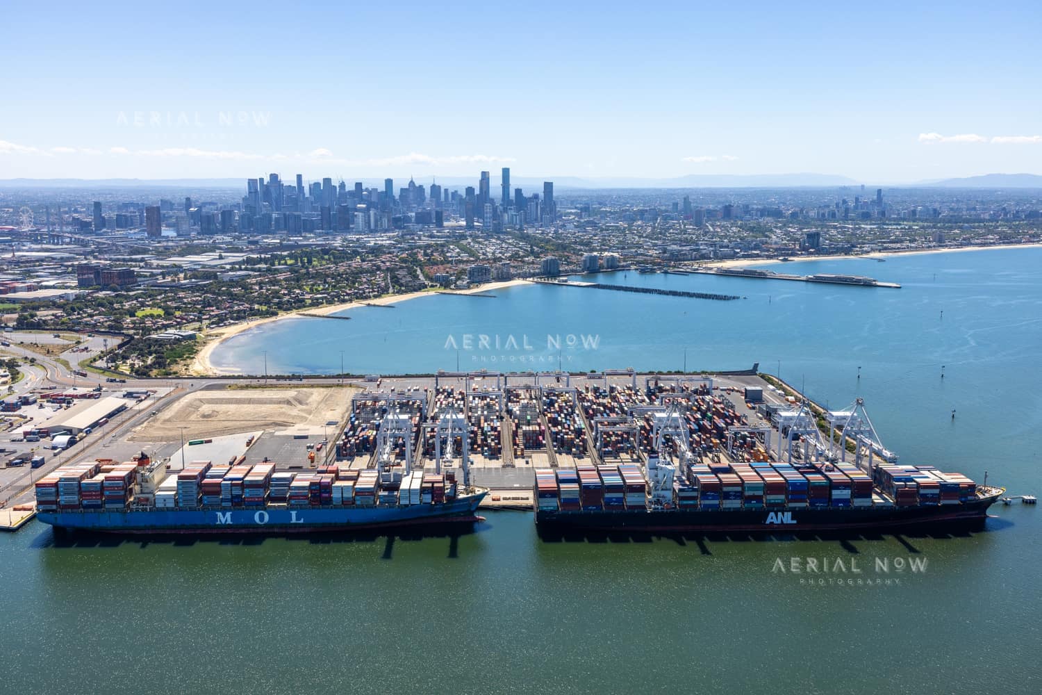 Aerial view across container ships and cranes at Webb Dock East towards the Melbourne skyline, Port Melbourne, in February 2022.