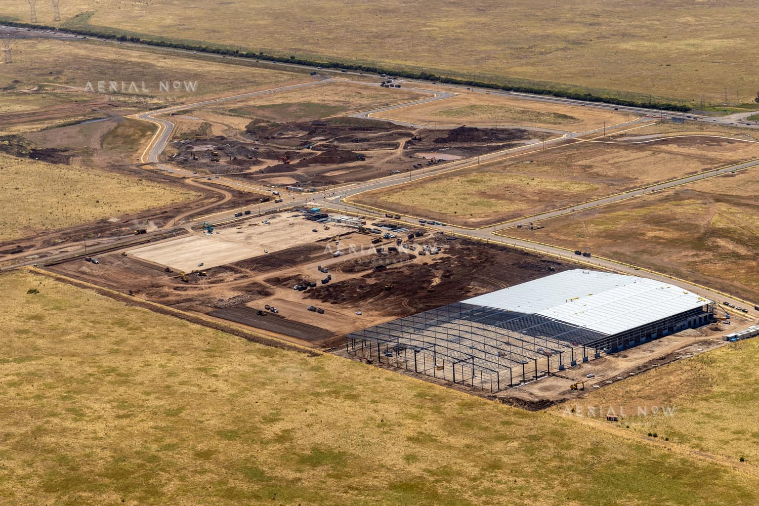 Aerial view of warehouse construction at Agar Industrial Estate Stage 4 on Middle Road, Truganina, showing steel framing, a partially roofed warehouse, earthworks, newly built estate roads and open land.