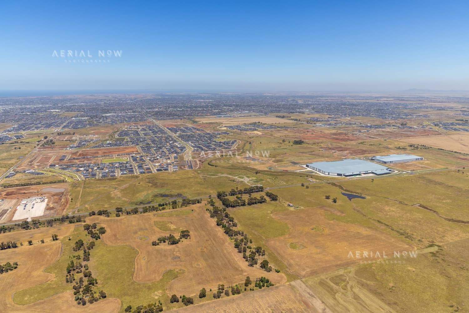Wide aerial view over Boundary Road in Truganina, showing established warehouses, expanding housing estates, open farmland and the future Djeembana logistics precinct in Melbourne's west.