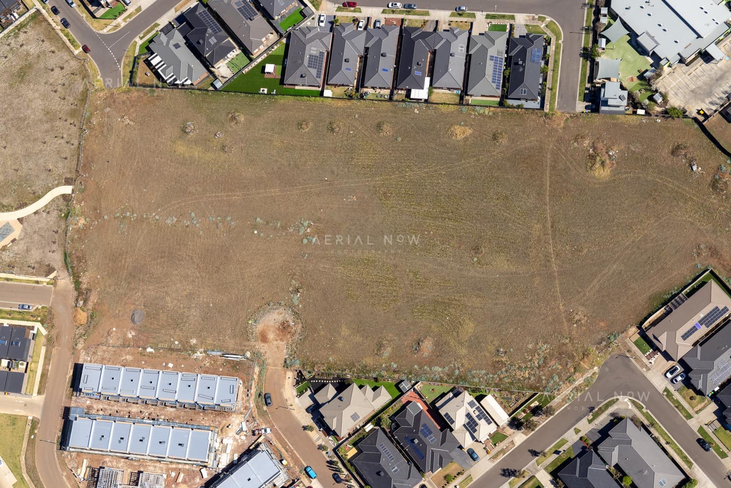 Aerial view of a vacant residential development site beside Agate Drive in Tarneit, Victoria, surrounded by new houses, roads and construction activity.