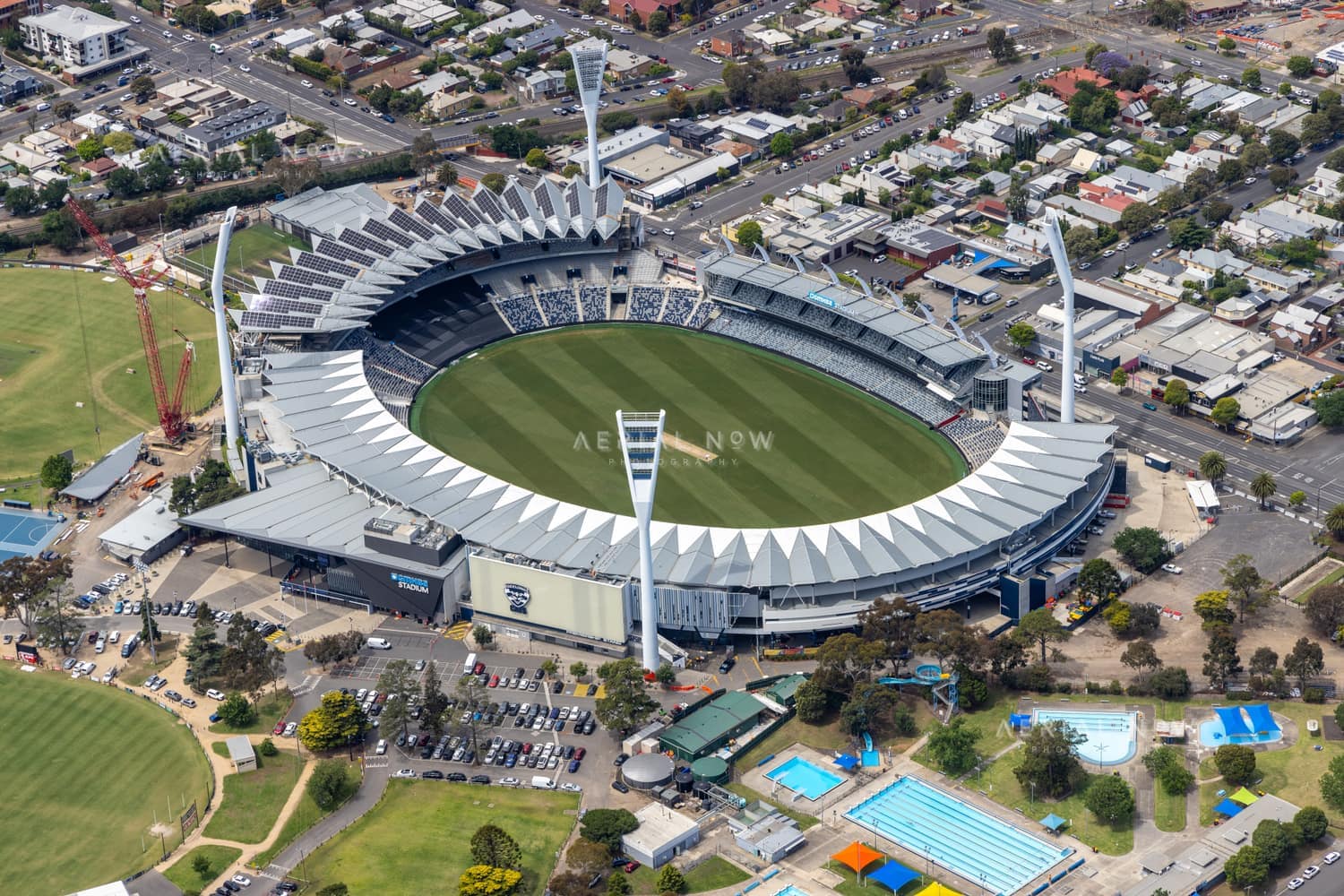 Aerial view of GMHBA Stadium at Kardinia Park in South Geelong, with the oval, grandstands, light towers, surrounding streets, car parks and nearby aquatic facilities visible.