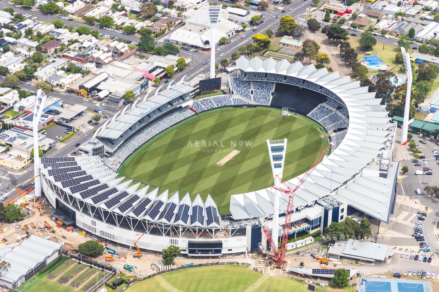 Aerial view of GMHBA Stadium at Kardinia Park in South Geelong, showing the oval, grandstands, cranes and redevelopment works beside surrounding streets and parkland.