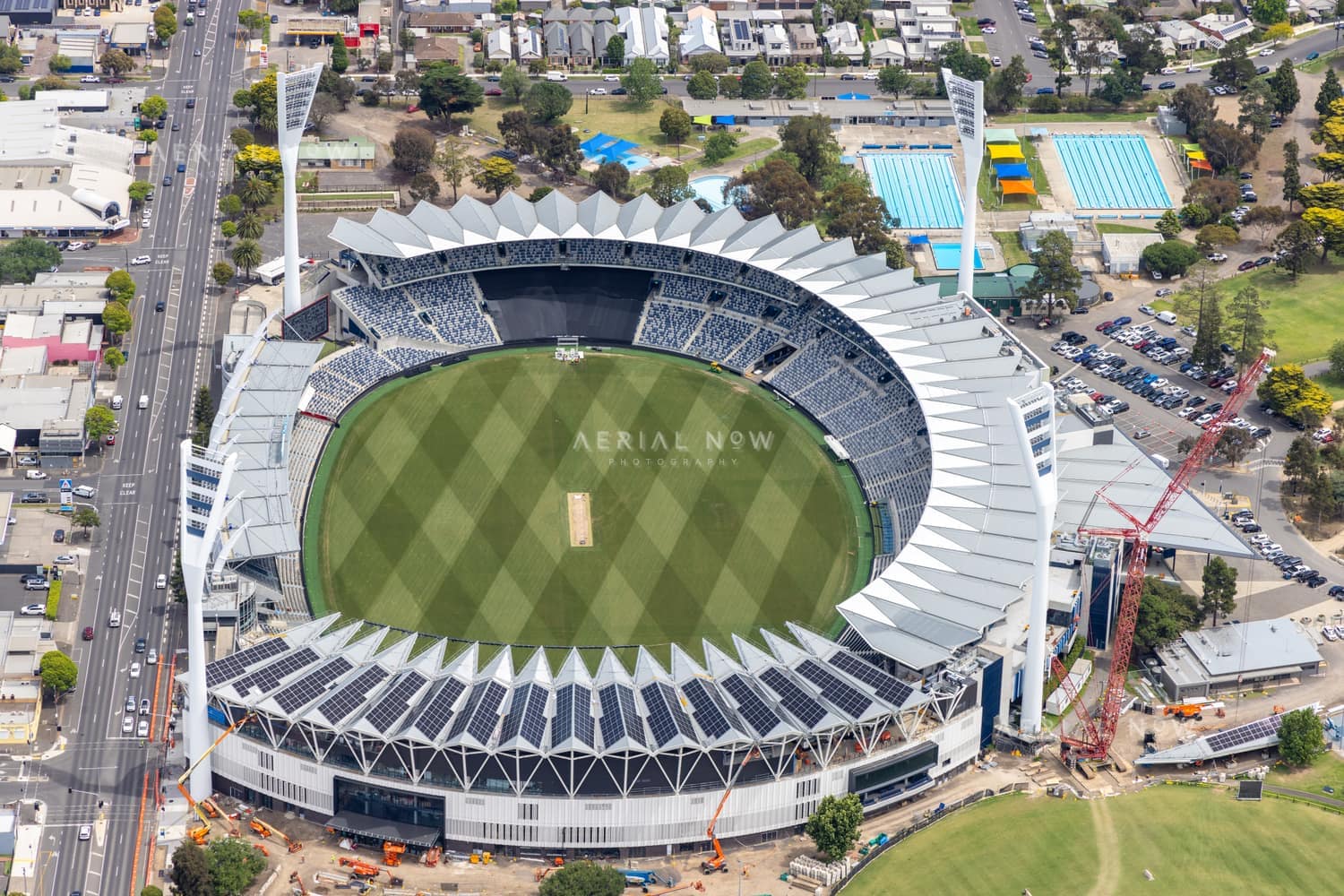 Aerial view of GMHBA Stadium at Kardinia Park in South Geelong, showing the oval, grandstands, light towers, nearby Moorabool Street, aquatic centre pools and construction activity.
