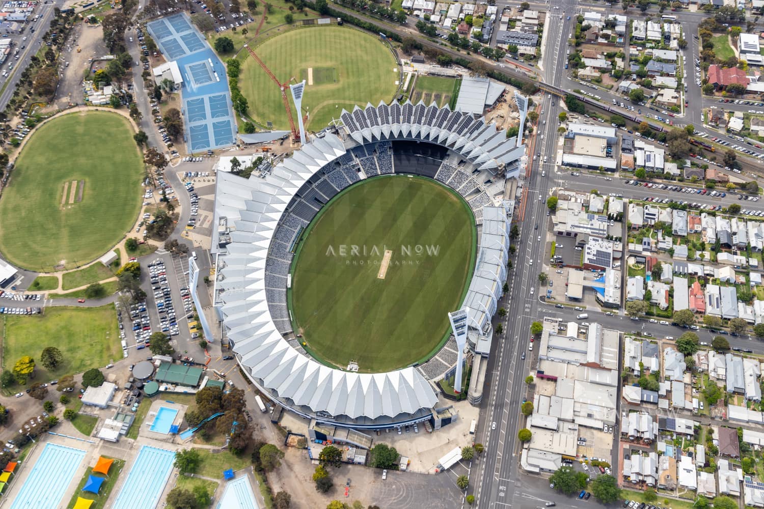 Aerial view of GMHBA Stadium at Kardinia Park in South Geelong, with the oval, grandstands, nearby sports fields, tennis courts, streets and surrounding residential blocks visible.