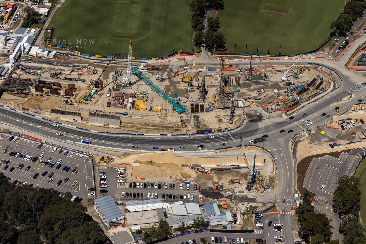 Aerial view of North East Link construction works along Bulleen Road in Bulleen, with cranes, roadworks, traffic lanes, car parks and sports fields visible.