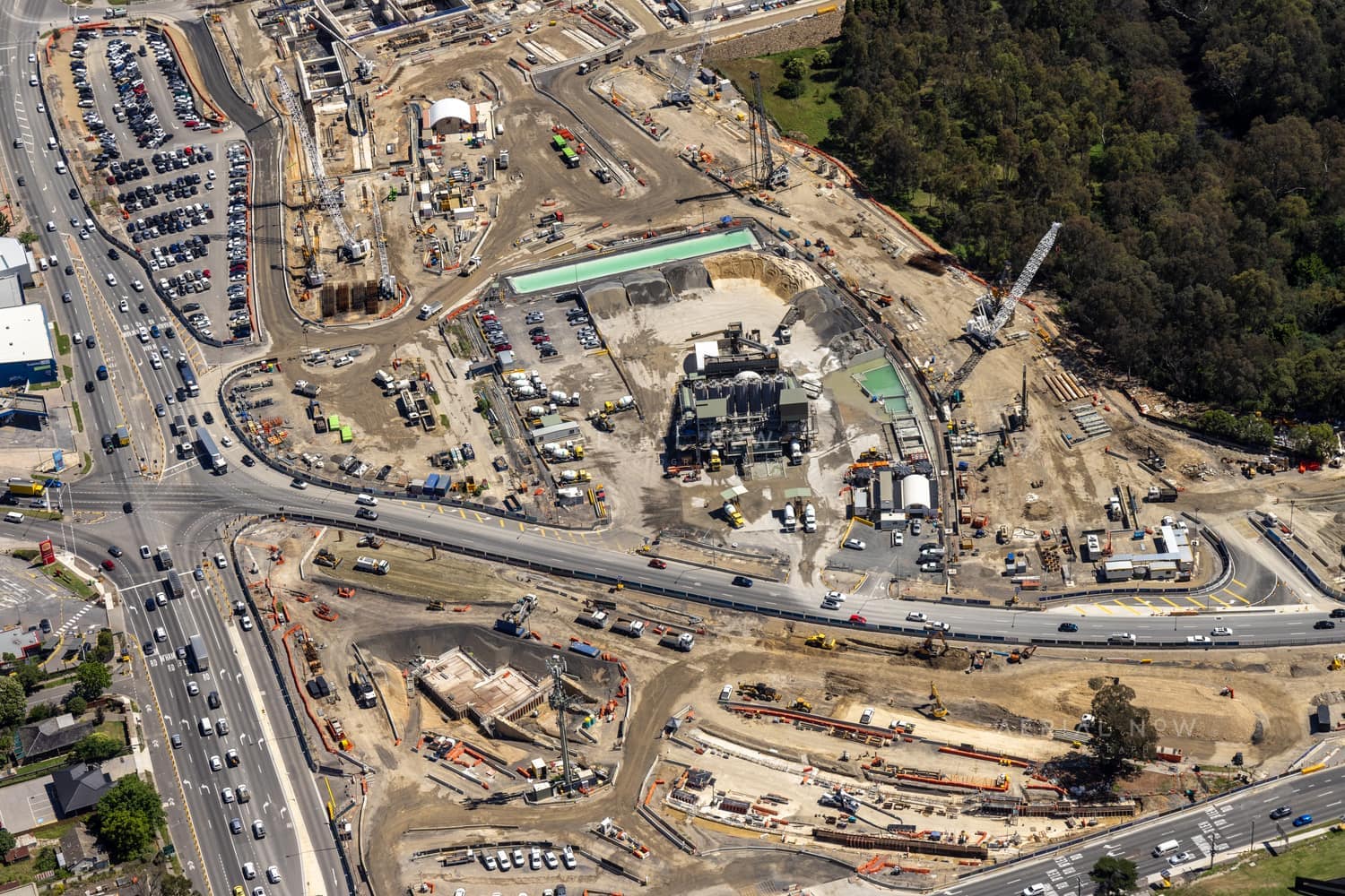 Aerial view of North East Link construction works in Bulleen, with major roadworks, cranes, machinery, site compounds and traffic on surrounding arterial roads.