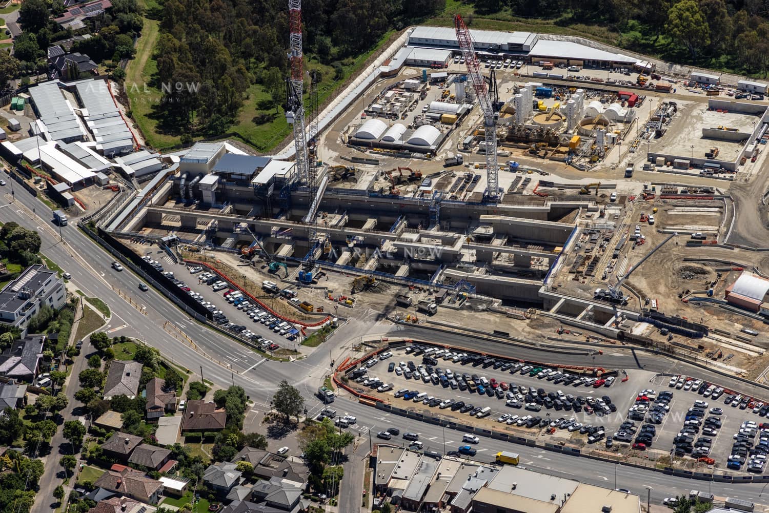 Aerial view of North East Link construction beside Bulleen Road in Bulleen, showing cranes, concrete works, traffic, parking areas and nearby homes.