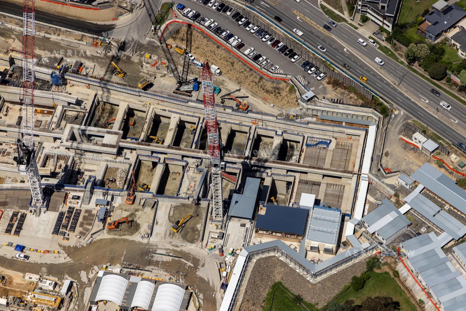 Aerial view of North East Link construction works in Bulleen with cranes, concrete structures, excavators, Bulleen Road traffic and nearby industrial buildings.
