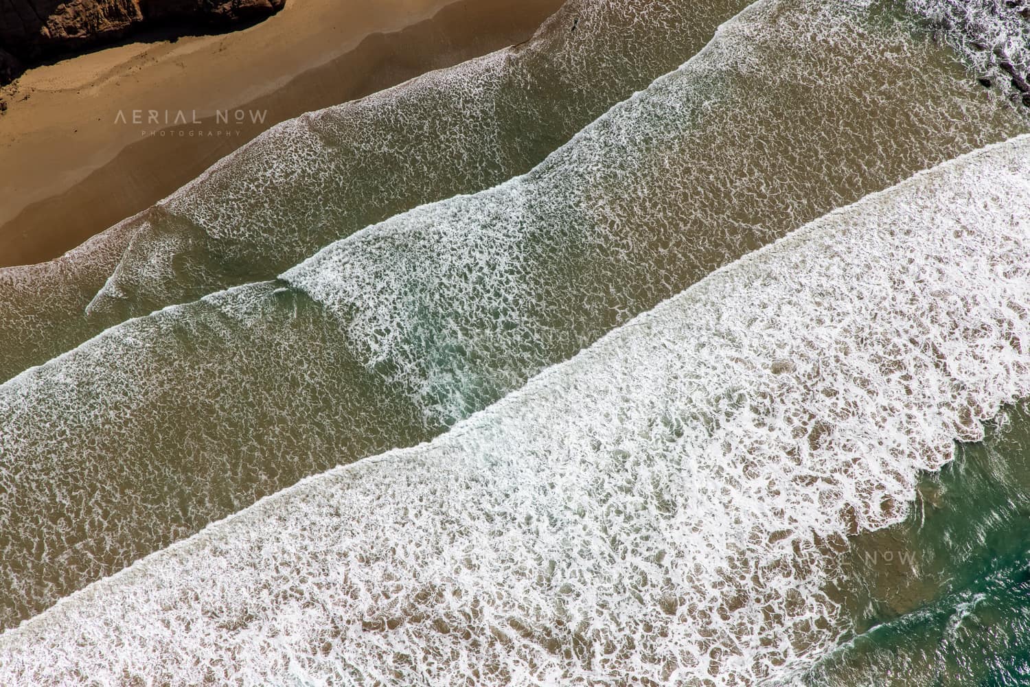 Aerial view of white surf breaking over shallow water beside a sandy beach on the Anglesea coastline in Victoria.