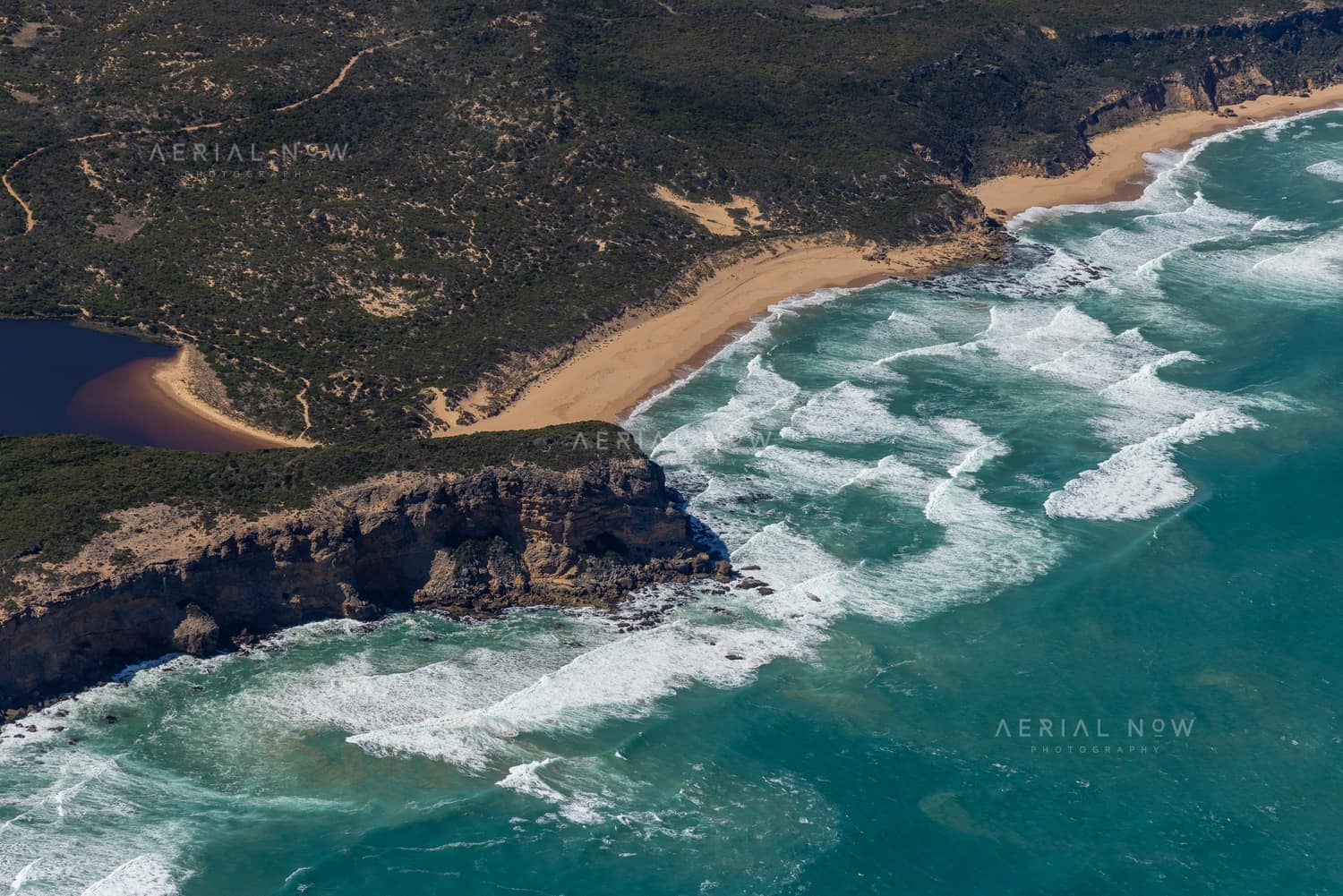 Aerial view of the Princetown coastline with surf breaking onto sandy beaches, a rocky headland, coastal scrub and a dark estuary near Princetown, Victoria.