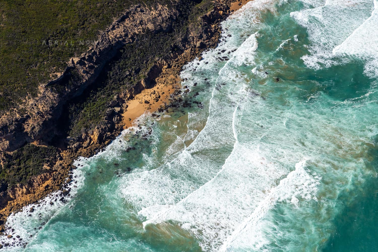 Aerial view of rugged cliffs, sandy coves and breaking surf along the Port Campbell National Park coastline near Princetown, Victoria.