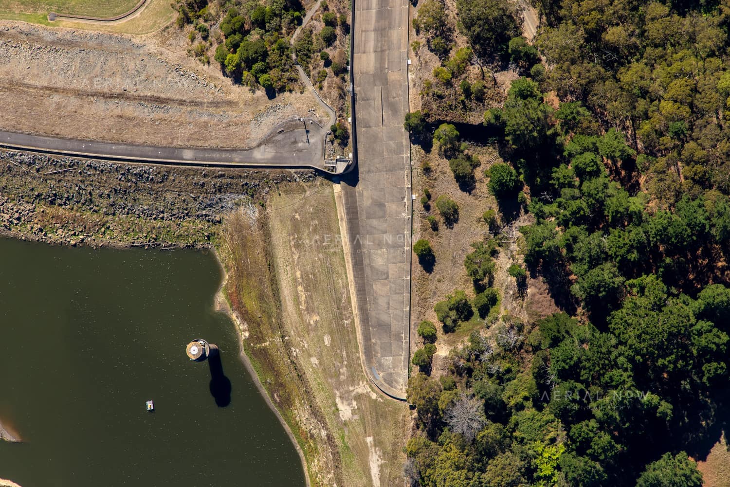 Aerial view of the West Barwon Reservoir dam wall at Forrest, showing the reservoir edge, concrete roadway and surrounding forest.
