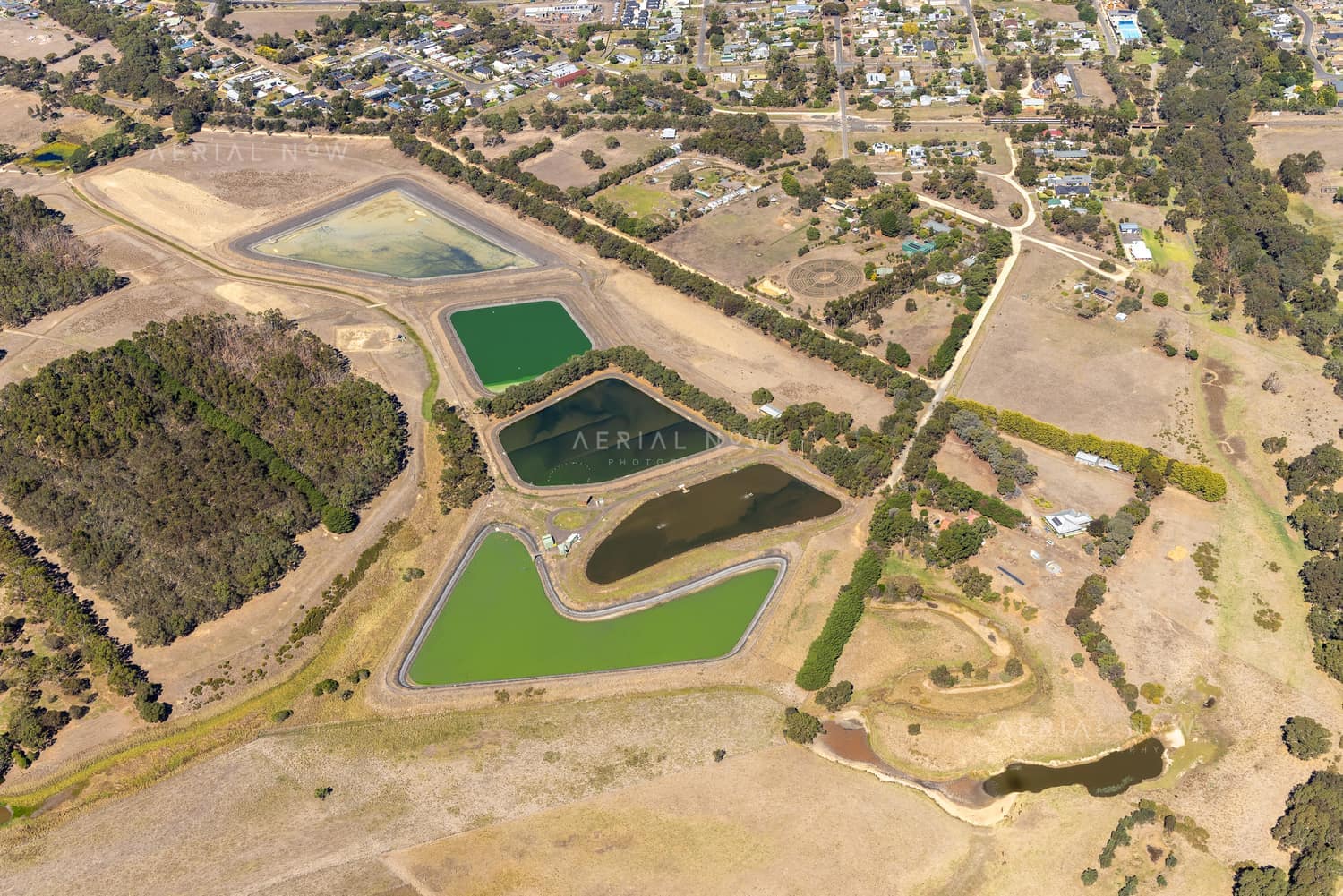 Aerial view of wastewater treatment ponds and service tracks on the edge of Winchelsea, VIC, with rural paddocks and township streets nearby.