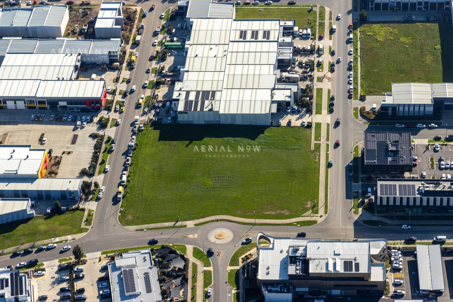 Aerial view of a vacant industrial land parcel surrounded by warehouses, commercial buildings, car parks and a roundabout in Clyde North, Victoria.