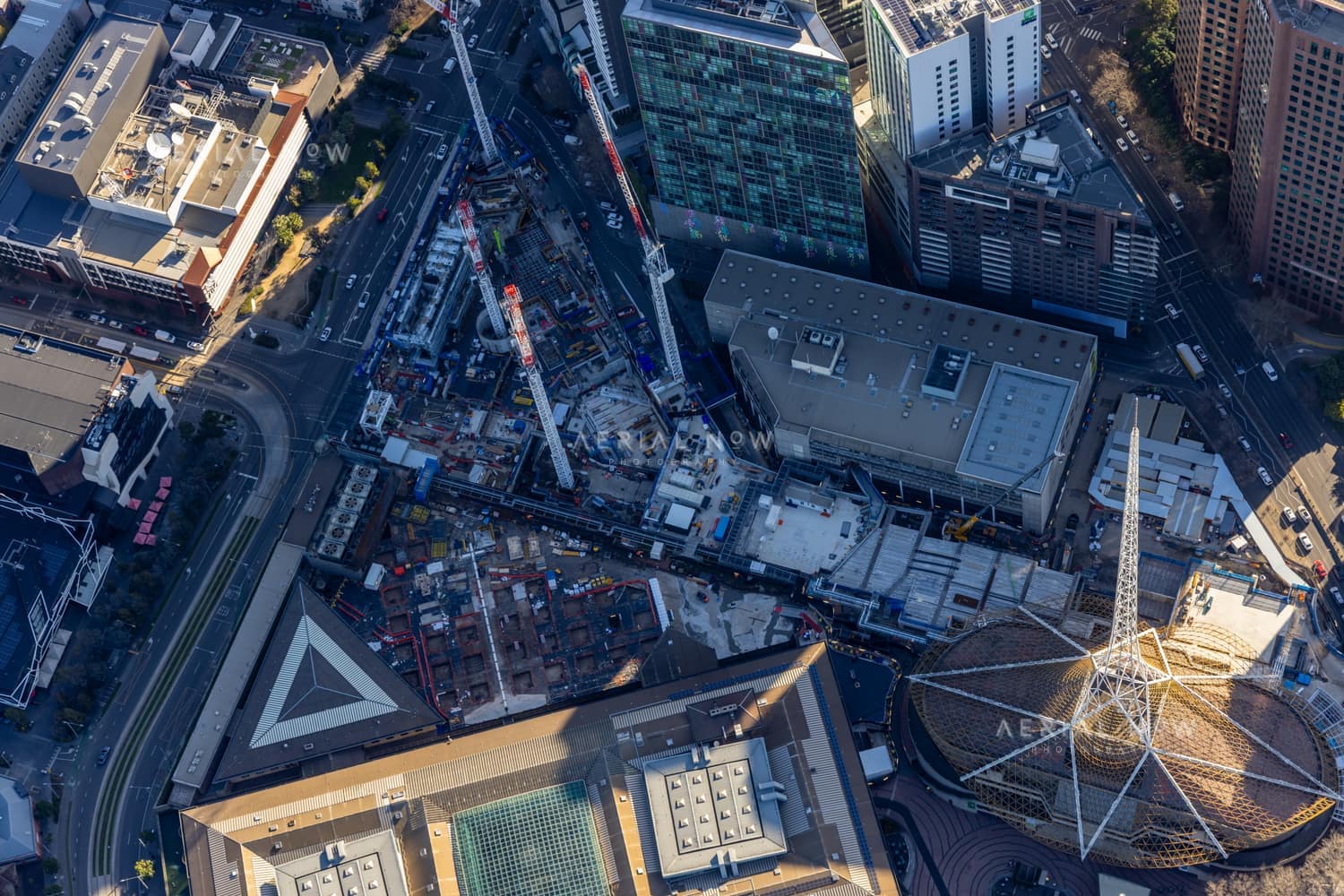 Aerial construction-progress view of the Melbourne Arts Precinct Transformation, with tower cranes, concrete works and the Arts Centre Melbourne spire in Southbank, Victoria.