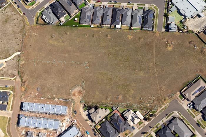 Aerial view of a vacant residential development site beside Agate Drive in Tarneit, Victoria, surrounded by new houses, roads and construction activity.