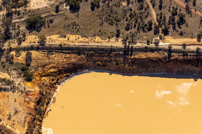 Aerial view of a muddy water storage dam edged by exposed earthworks, dirt tracks and scattered rural vegetation in Melton, Victoria.
