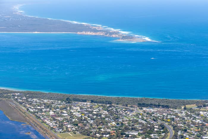 Aerial view of Point Lonsdale residential streets and coastal vegetation beside blue water, with Point Nepean visible across Port Phillip Bay.