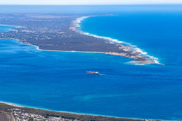 Aerial view of Port Phillip Heads and Point Nepean from Point Lonsdale, with a cargo ship crossing blue water between the coastline and surf beaches.