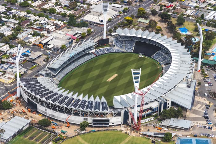 Aerial view of GMHBA Stadium at Kardinia Park in South Geelong, showing the oval playing field, grandstands, light towers, cranes and surrounding streets.