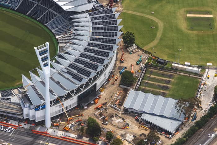 Aerial view of GMHBA Stadium at Kardinia Park in South Geelong, showing grandstand roof solar panels, a light tower, surrounding sports fields and active construction works.