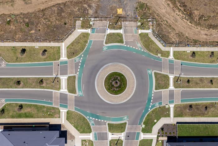 Aerial view of a landscaped roundabout with bike lanes, pedestrian crossings, footpaths and surrounding residential lots in Mickleham, Victoria.