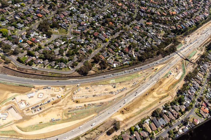 Aerial view of North East Link construction works in Watsonia North, with road lanes, earthworks, machinery, traffic and surrounding residential streets visible.