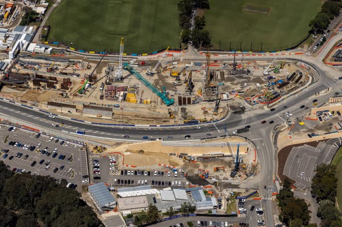 Aerial view of North East Link construction works along Bulleen Road in Bulleen, with cranes, roadworks, traffic lanes, car parks and sports fields visible.