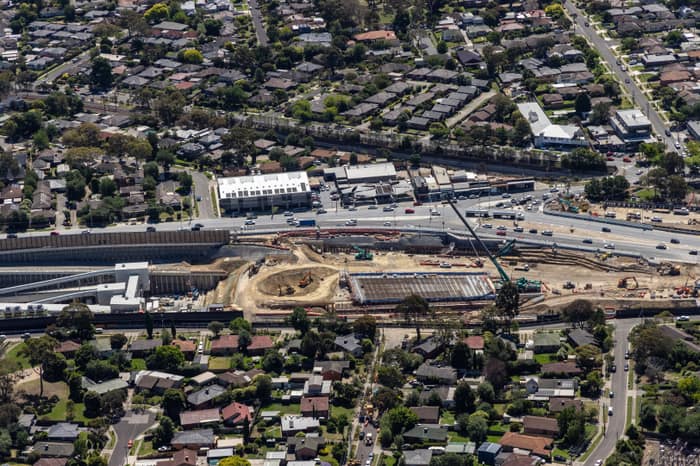 Aerial view of North East Link construction works beside Service Road in Watsonia, with excavation areas, retaining walls, traffic and surrounding suburban streets.
